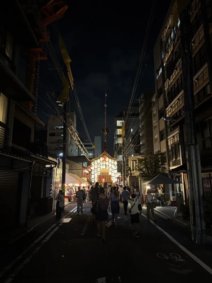 A Gion Matsuri float glowing with lanterns at the end of a quiet Kyoto street at night