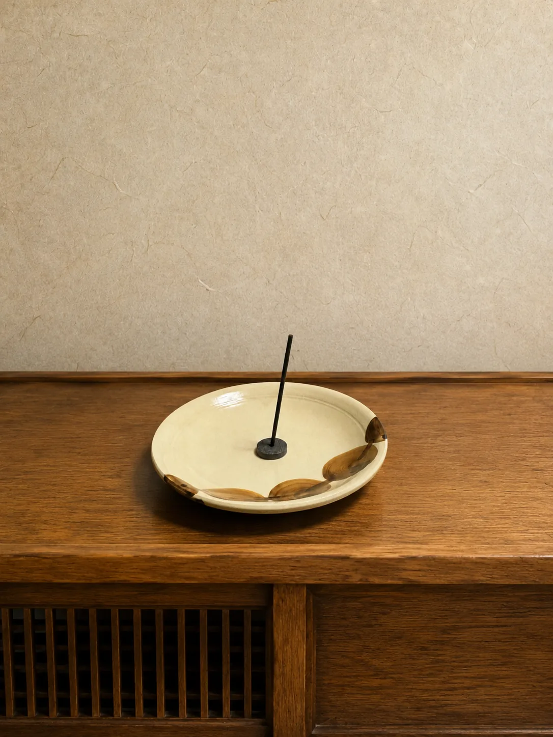 A single incense stick standing in a handmade ceramic dish on a wooden tansu chest
