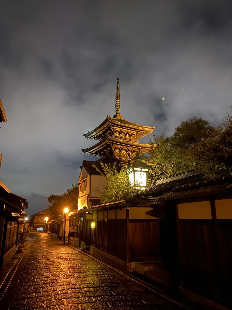 The Yasaka Pagoda lit gold at night above the wet stone lane of Ninenzaka in Higashiyama, Kyoto